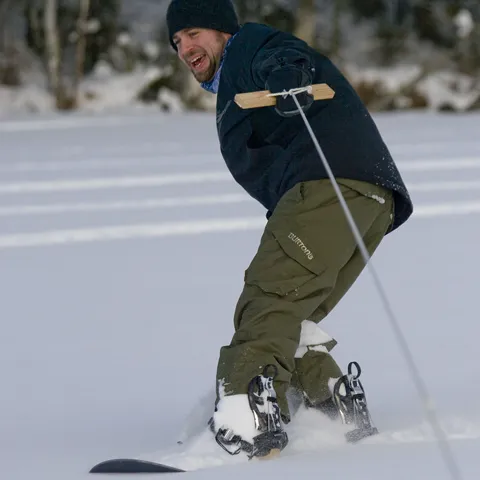 Jared snowboarding mid-action, towed across a snowy field, grinning.